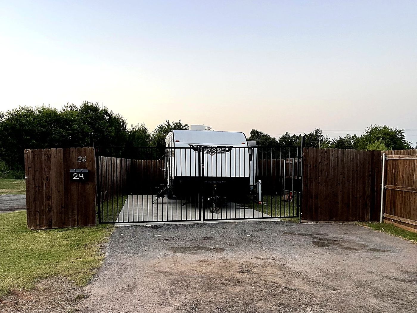 Travel trailer on a fenced and gated site at dusk, gate closed